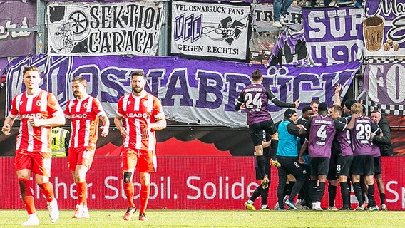 Spieler vom VfL Osnabrück bejubeln im Hintergrund einen Treffer gegen Energie Cottbus. © IMAGO / Fotostand 