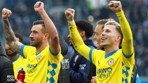 Eintracht Braunschweigs Profis Robin Krauße (l.) und Lino Tempelmann reißen jubelnd die Arme hoch. © IMAGO / Jan Huebner 