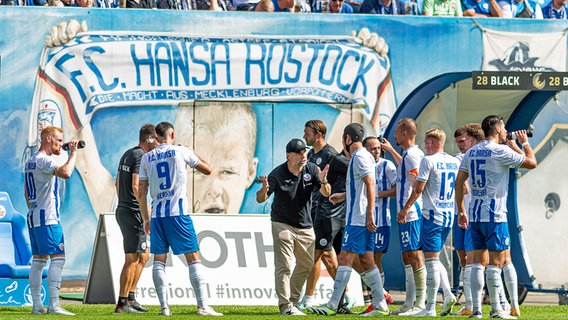 Die Spieler des FC Hansa Rostock stehen zusammen mit Trainer Bernd Hollerbach (MItte) auf dem Rasen © picture alliance / Fotostand 