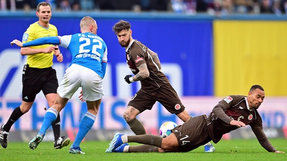 Rostocks Japser van der Werff (l.) versucht, gegen St. Paulis Marcel Hartel (M.) und Etienne Amenyido den Ball zu bekommen. © Witters 