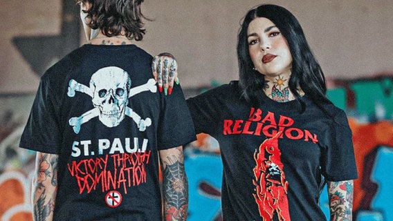 Eine Frau und ein Mann präsentieren die "Bad Religion"-T-Shirts des FC St. Pauli. © FC St. Pauli 