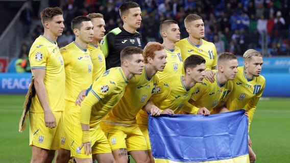 Die ukrainischen Nationalspieler posieren vor Spielbeginn mit einer Nationalflagge. © IMAGO / Sportimage 