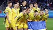 Die ukrainischen Nationalspieler posieren vor Spielbeginn mit einer Nationalflagge. © IMAGO / Sportimage 