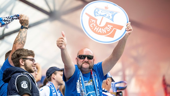 Ein Rostock-Fan hält ein großes Hansa-Logo hoch. © IMAGO / Fotostand 