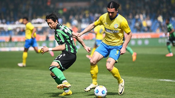 Hannovers Sei Muroya (l.) und Braunschweigs Rayan Philippe kämpfen um den Ball. © picture alliance/dpa | Swen Pförtner 