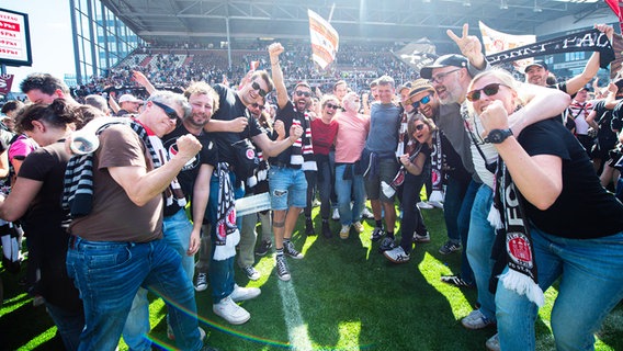 Fans des FC St. Paulis feiern den Bundesliga-Aufstieg auf dem Spielfeld. © IMAGO / Noah Wedel 