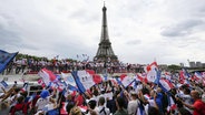 Menschen versammeln sich an der Pariser Seine und schwenken französische Fahnen. © IMAGO / Kyodo News 