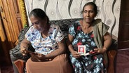 Zwei Frauen sitzen auf einem Sofa und halten ein Foto ihrer vermissten Kinder in Sri Lanka © NDR Foto: Charlotte Horn