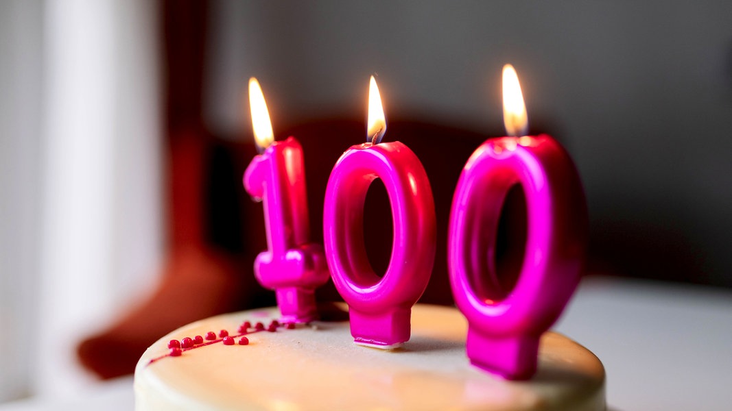 Auf einer Torte brennen Kerzen in der Form der Zahl 100.