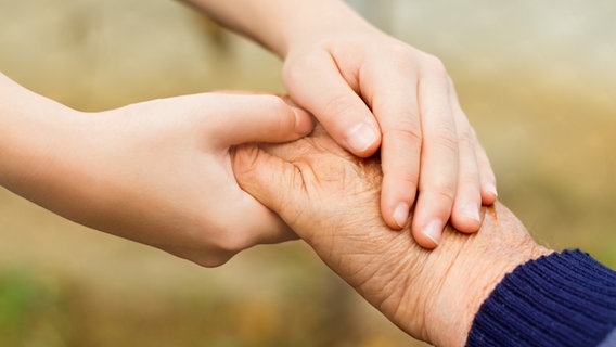 Die Hände eines jungen Menschen umfassen die Hand eines alten Menschen. © Colourbox 