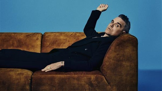 Robbie Williams liegt auf einem Sofa und schaut in die Kamera © MCT Agentur GmbH, Netflix Foto: MCT Agentur GmbH, Netflix