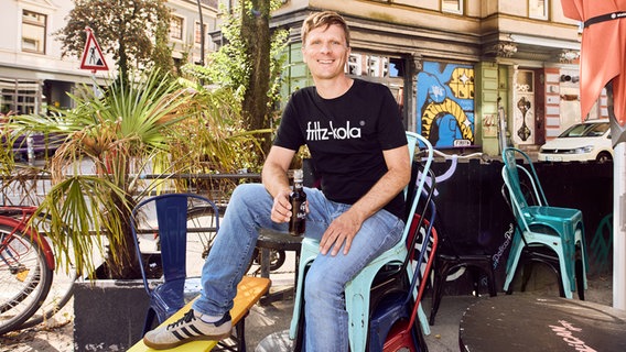 Mirco Wiegert sitzt auf einem Plastikstuhl und hält eine Flasche fritz-kola in der Hand © fritz-kola 