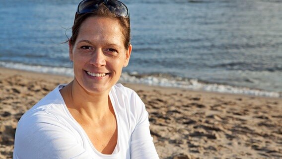 Olympiasiegerin Sandra Völker sitzt lächelnd am Strand. © Kommunikation GmbH 