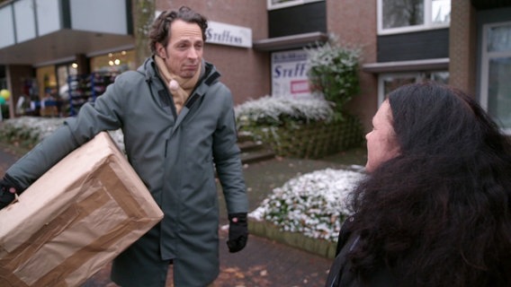 Jo Hiller mit einem großen Paket unterm Arm interviewt eine Passantin. © Screenshot 