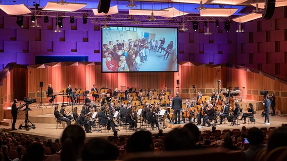 Konzert der Orchester-Detektive: Die NDR Radiophilharmonie, auf der Leinwand eine Schulklasse im Klassenzimmer © NDR Foto: Micha Neugebauer