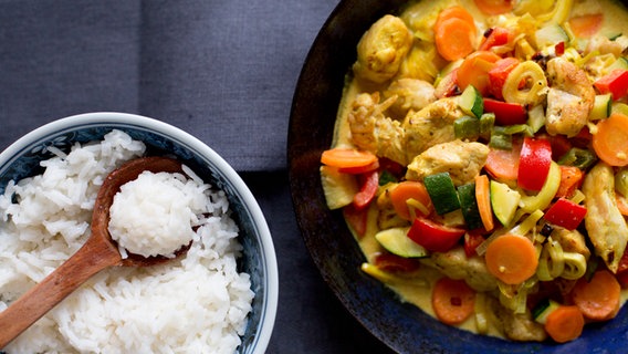 Gemüse-Putencurry in einer Pfanne und eine Schüssel mit Reis stehen auf dem Tisch. © NDR Foto: Claudia Timmann